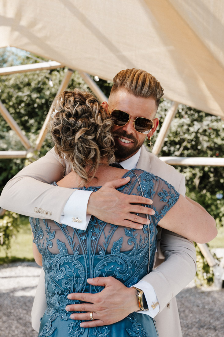 Mann umarmt Frau in blauem Kleid mit Manschettenknöpfen und Sonnenbrille