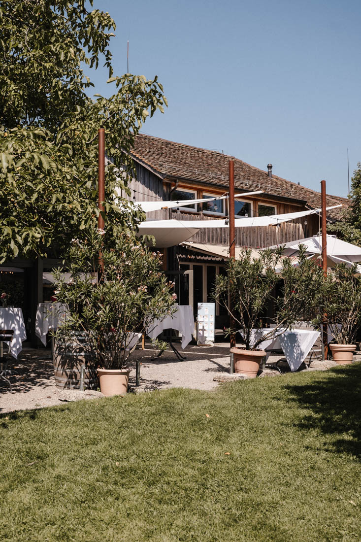Aussenbereich mit Tischen und weissen Decken bei Holzhaus und Bäumen