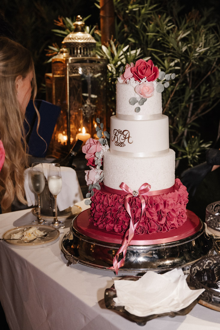 Vierstöckige Torte mit Rosen und Initialen steht auf Tisch mit Gläsern