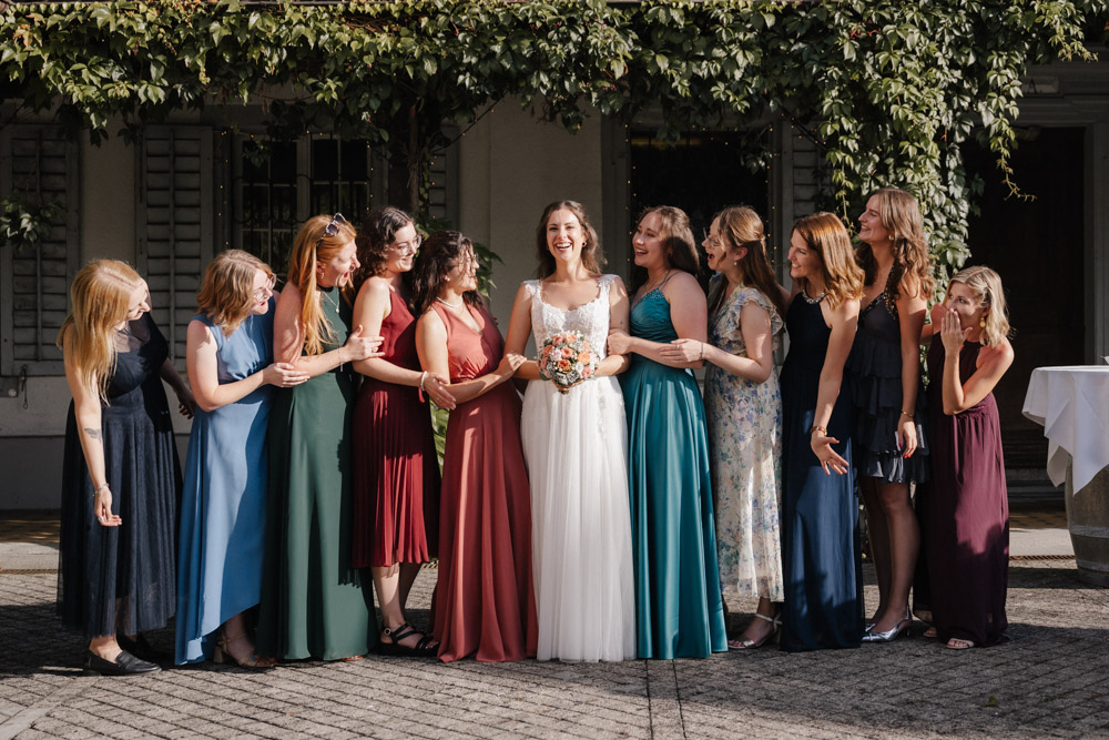Braut mit Blumenstrauss und Frauen in farbigen Kleidern lächeln