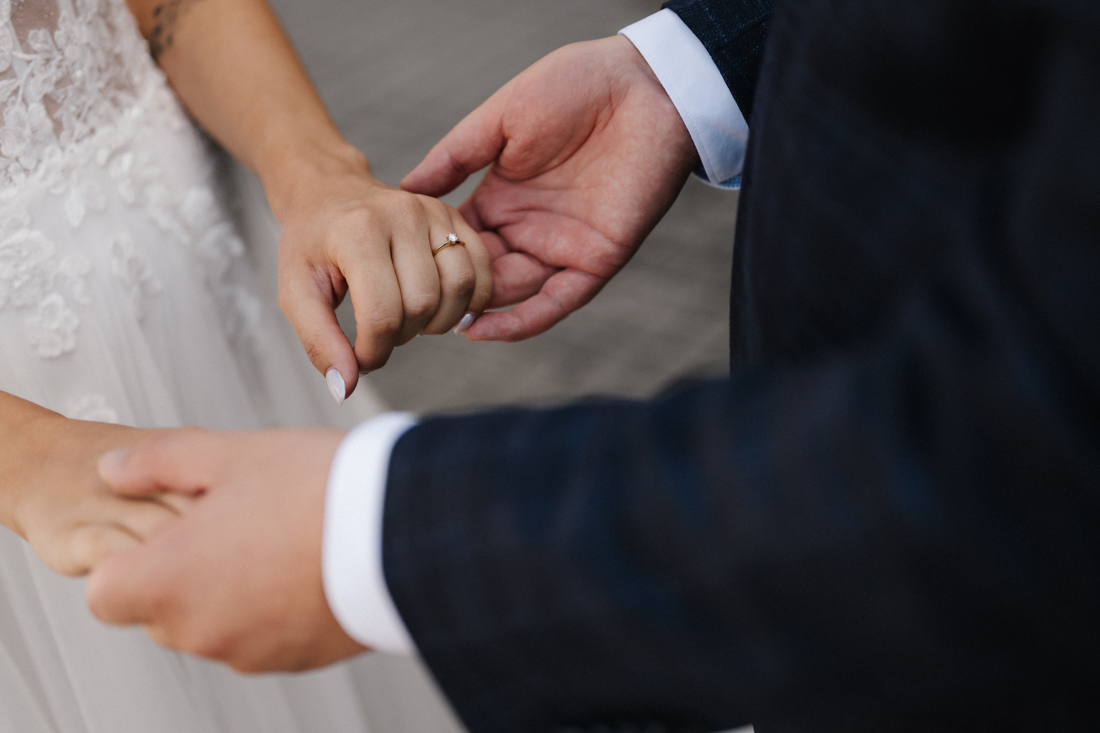 Hände halten sich mit Ring bei weissem Kleid und Anzug
