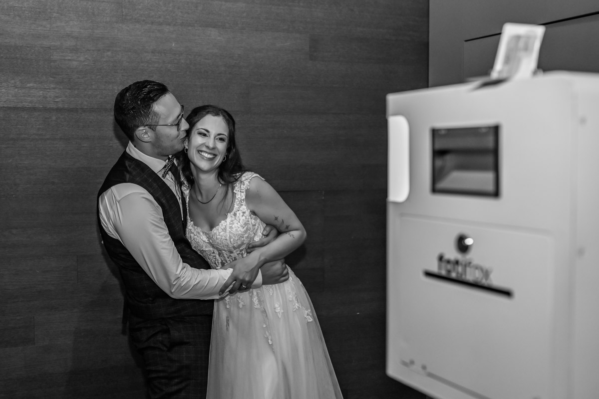Mann küsst Frau mit Kleid und Fotobox im Hintergrund schwarzweiss