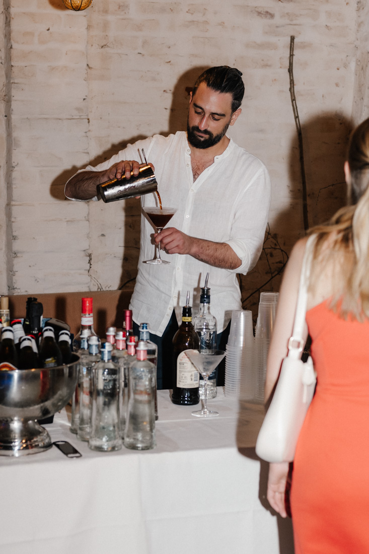 Barkeeper giesst Drink in Glas mit Flaschen und Frau im Vordergrund