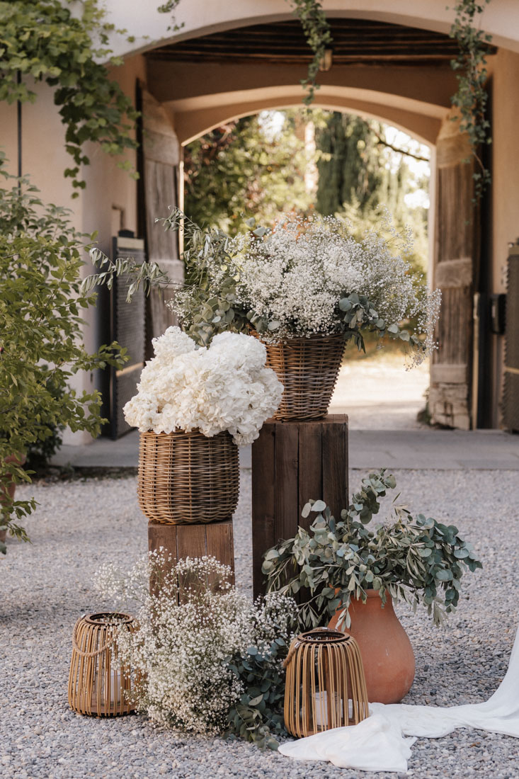 Blumen in Körben und Laternen vor Holztor und Steinboden im Freien