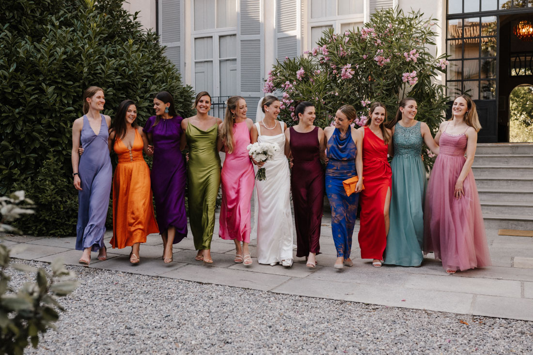 Braut mit Blumenstrauss und Freundinnen in bunten Kleidern auf Weg