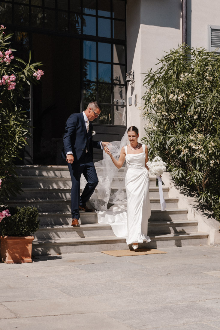 Braut mit Schleier und Blumenstrauss geht mit Mann Treppe runter