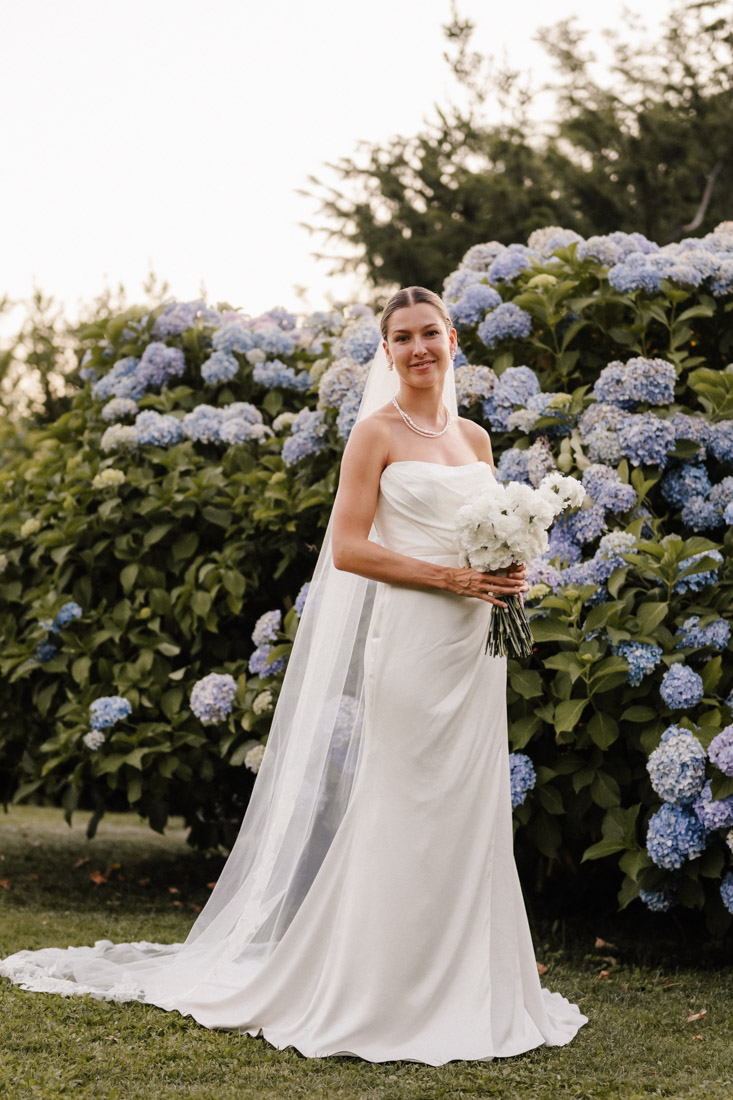 Frau mit Schleier und weissem Kleid mit Blumenstrauss vor Hortensien