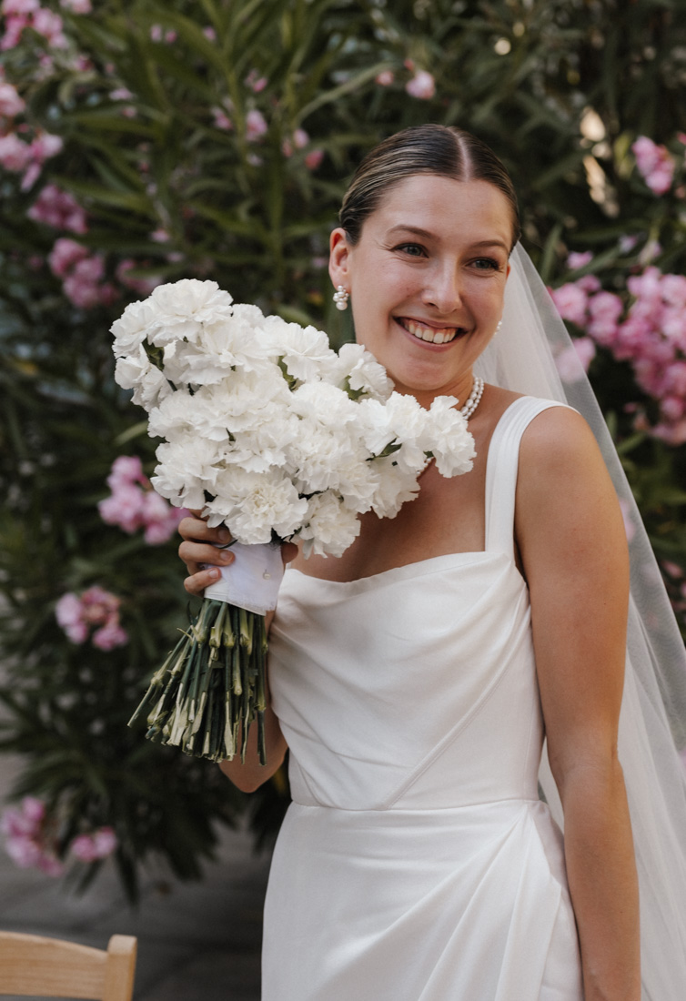 Frau im weissen Kleid mit Blumenstrauss und Schleier lächelt