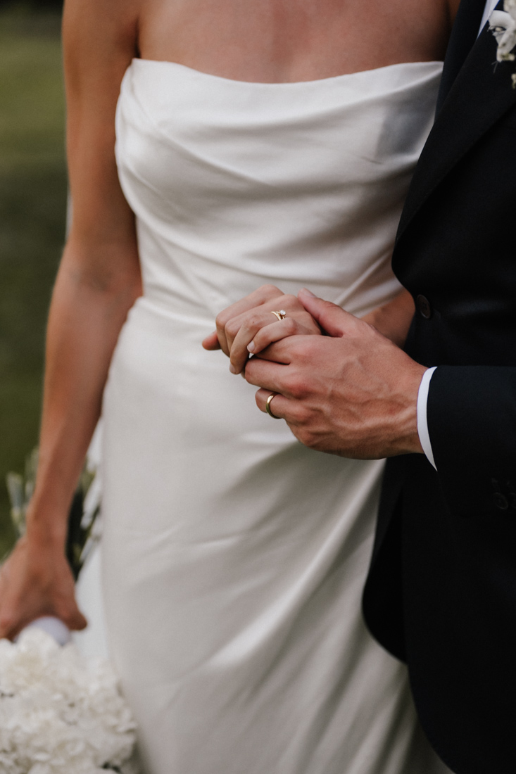 Braut im weissen Kleid und Bräutigam mit Anzug halten Hände mit Ringen