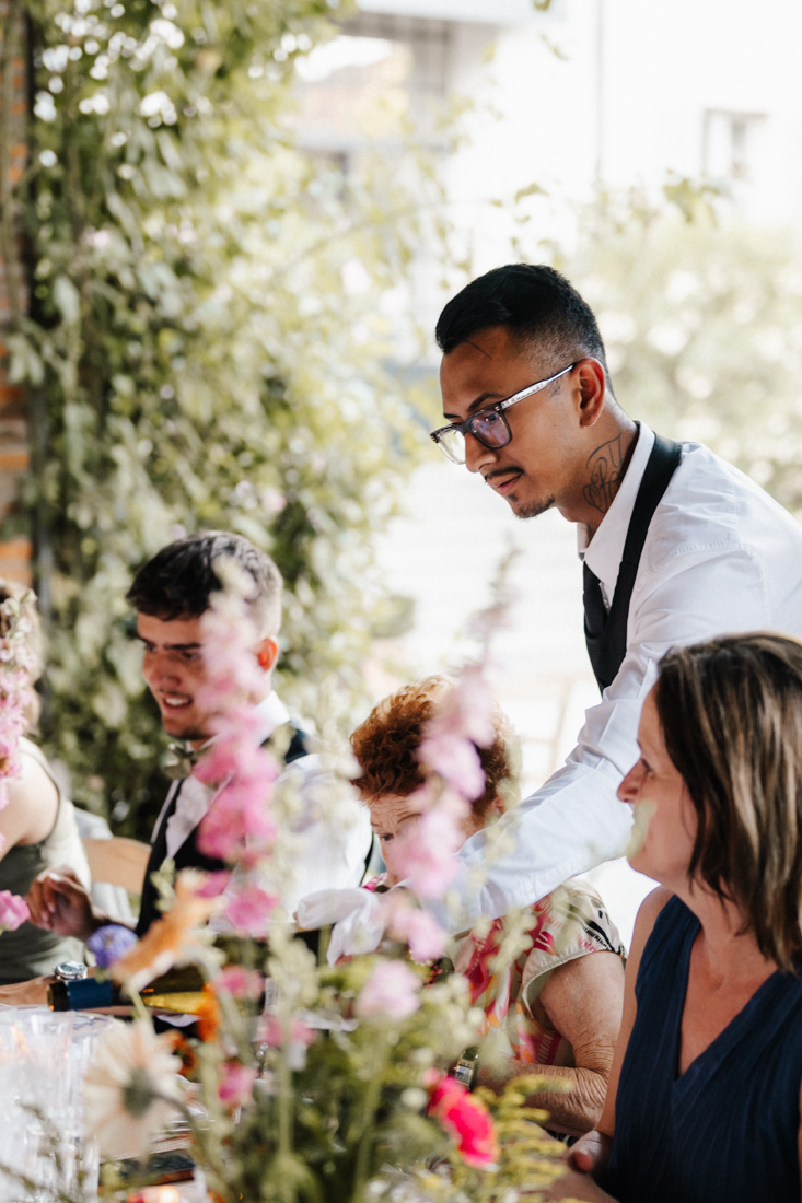 Kellner bedient Gaeste bei Tisch mit Blumen und Pflanzen