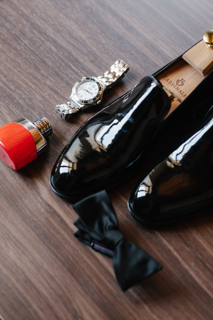 Lackschuhe mit Uhr und Fliege sowie Parfum auf braunem Holz