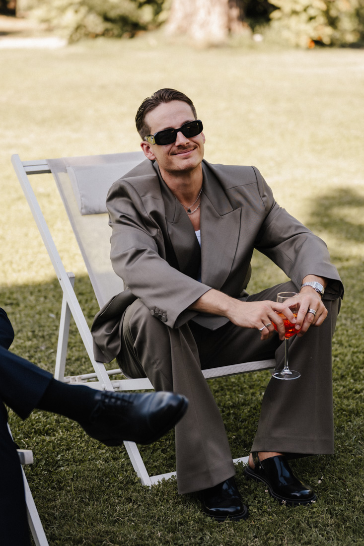 Mann mit Sonnenbrille sitzt mit Drink und Anzug auf Liegestuhl