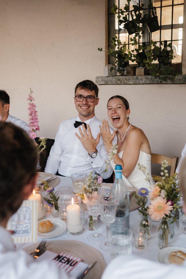 Mann mit Brille und Frau zeigen Eheringe am Tisch mit Blumen