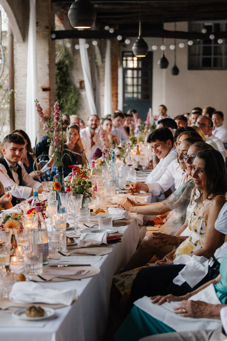 Menschen sitzen an langer Tafel mit Blumen und Gläsern