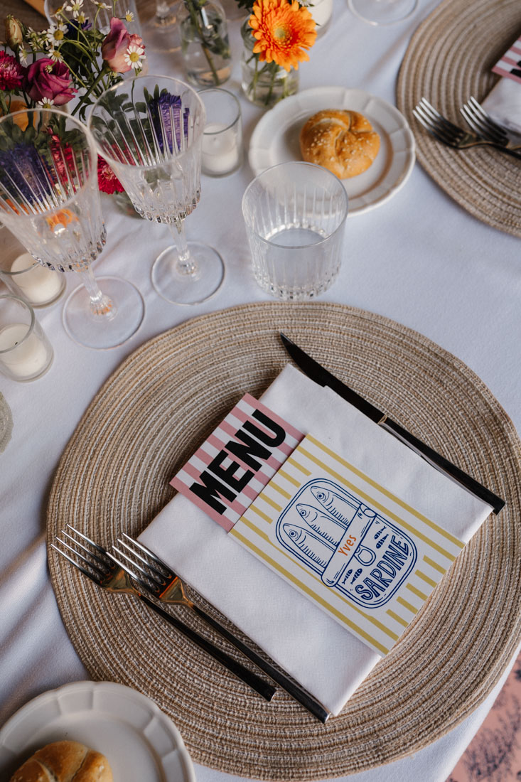 Gedeckter Tisch mit Menu Karte Serviette Besteck Glas und Blumen