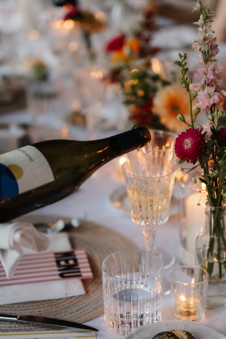 Weinflasche wird in Glas gefuellt mit Blumen und Kerzen