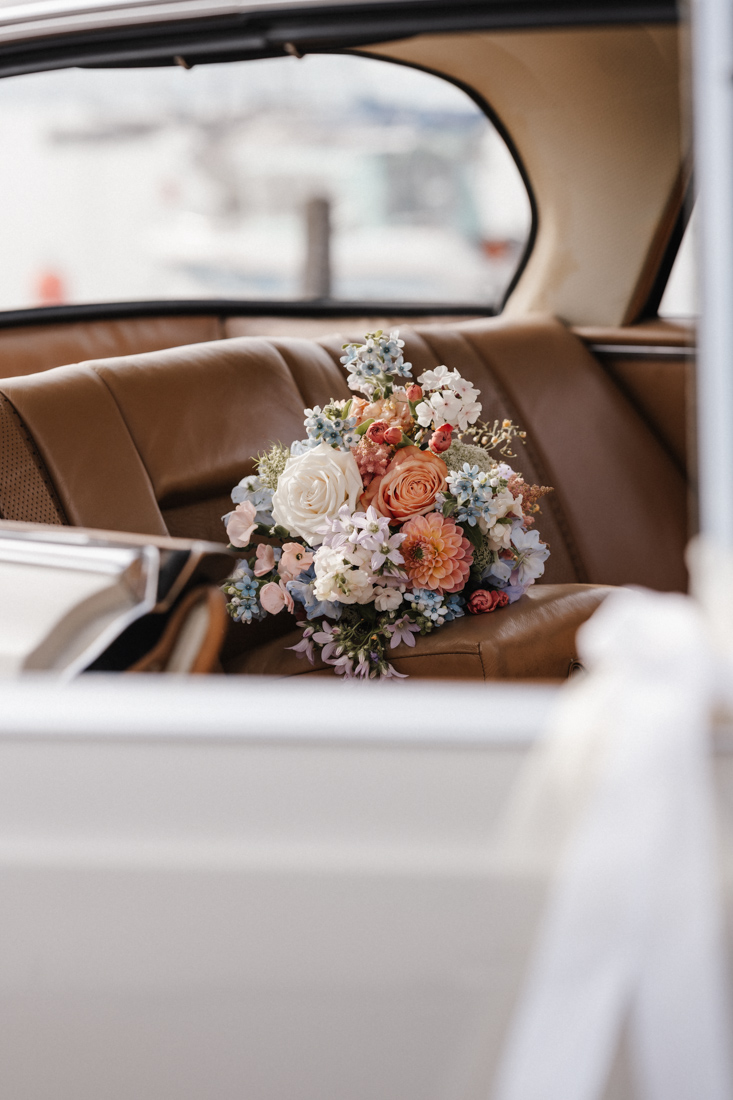Blumenstrauss liegt auf brauner Ledersitzbank im Auto mit weisser Schleife