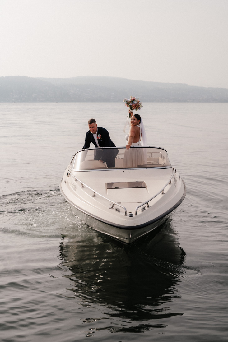 Brautpaar auf weissem Motorboot mit See und Bergen im Hintergrund