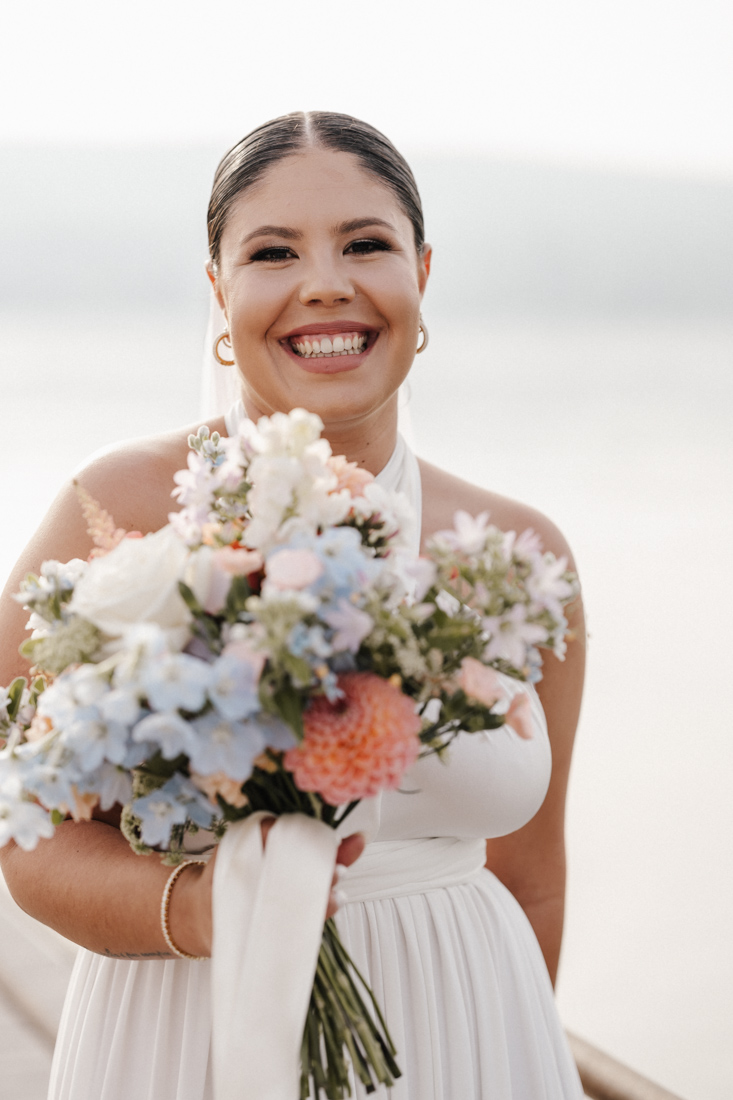 Frau in weissem Kleid lächelt mit Blumenstrauss in der Hand