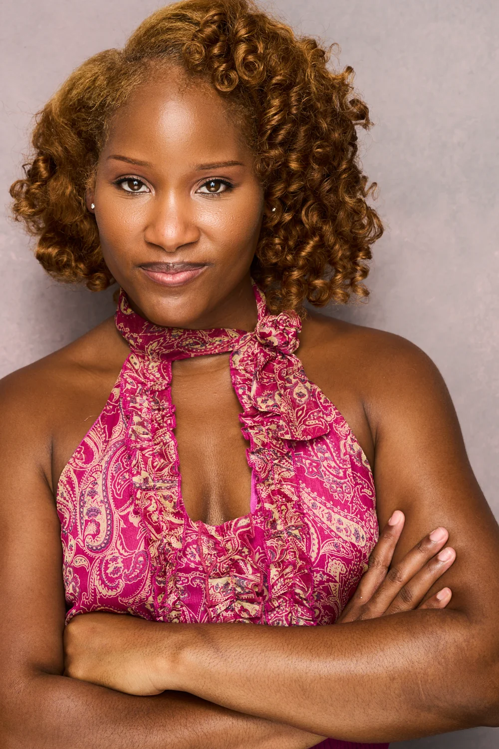 Marie Wilde beaming in a pink top with a single fastened overall strap, framed by curly hair on lavender background
