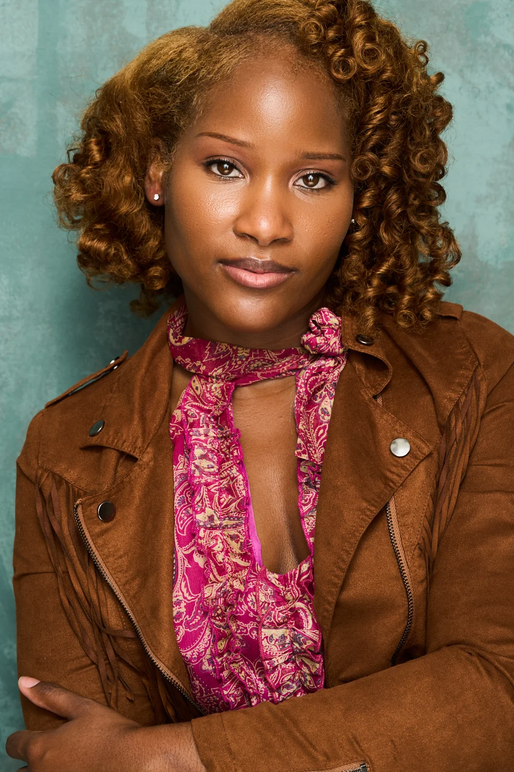 Marie Wilde in three-quarters profile wearing an orange ribbed turtleneck against a mottled brown background