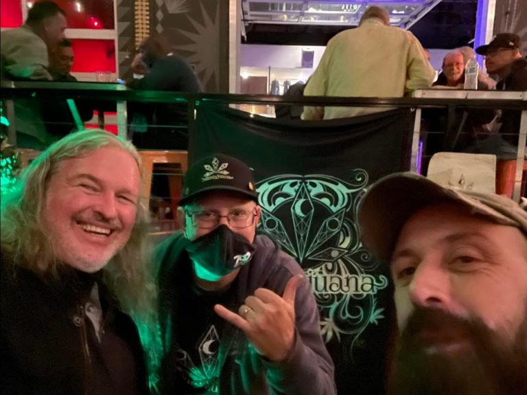 Three people posing together indoors with a Martyjuana banner behind them