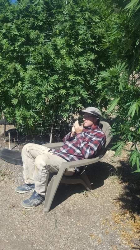 Marty Clein sitting in a chair outdoors beside tall green plants