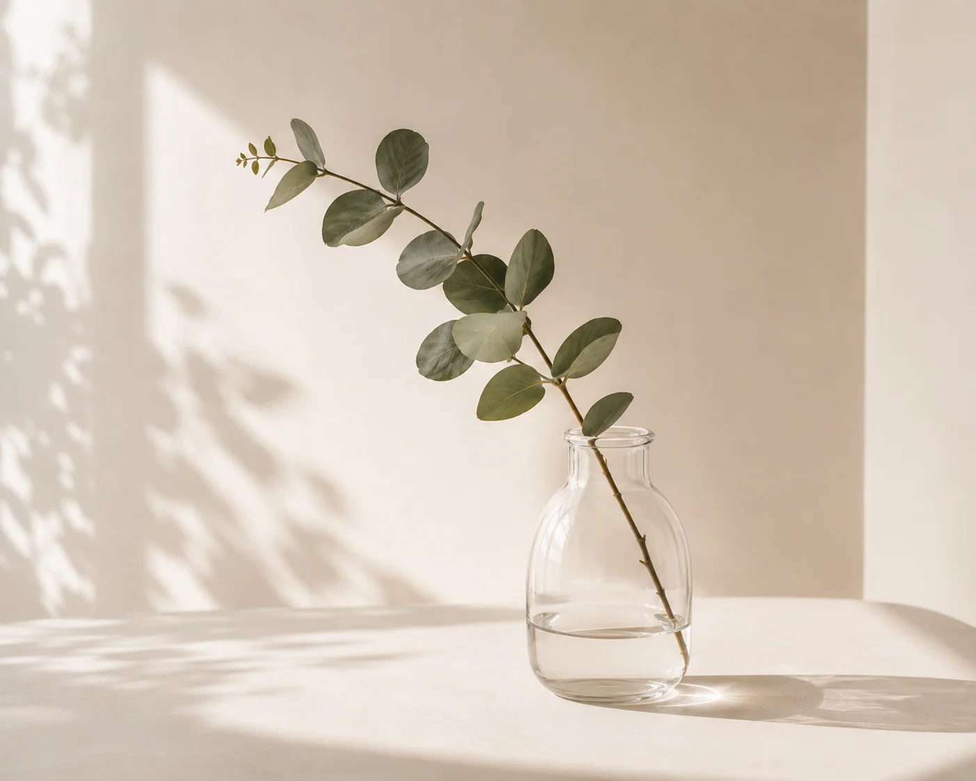A green journal and gold pen on a desk with a water glass and eucalyptus branches