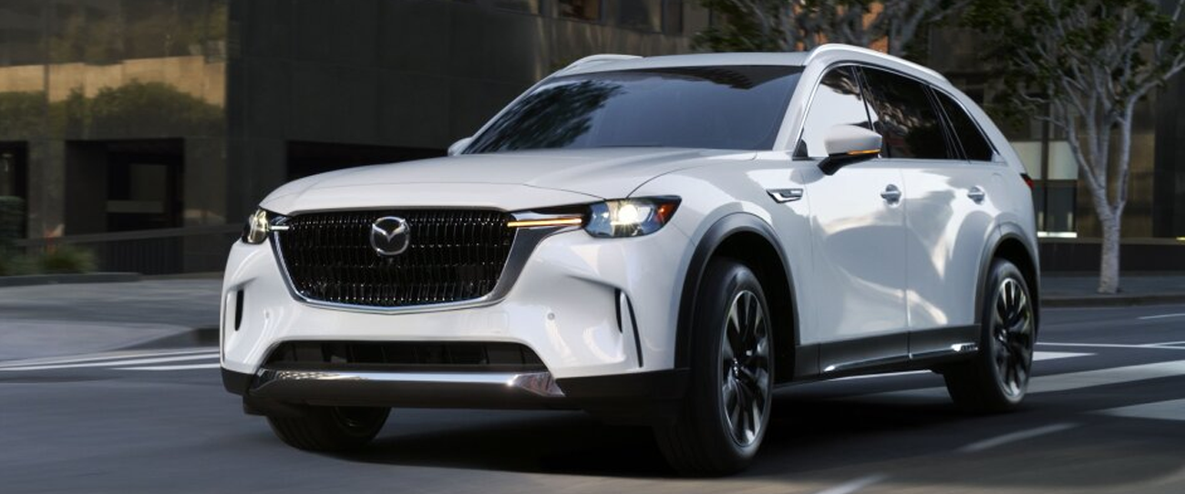 Vue 3/4 avant et latérale d'une Mazda Hybride CX-90 2025 roulant a une intersection