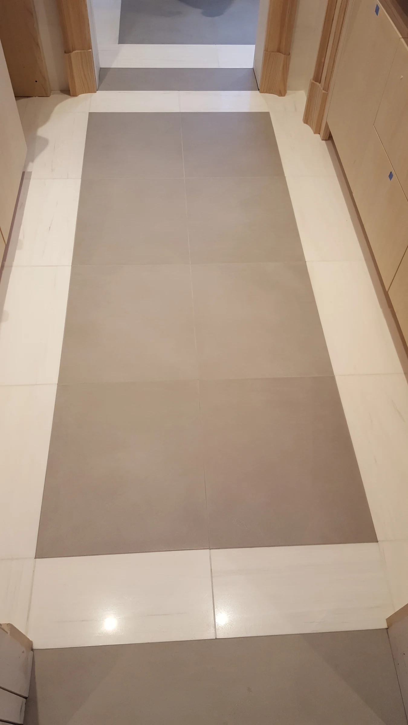 Rectangular taupe floor tiles framed by a light-colored border during installation.