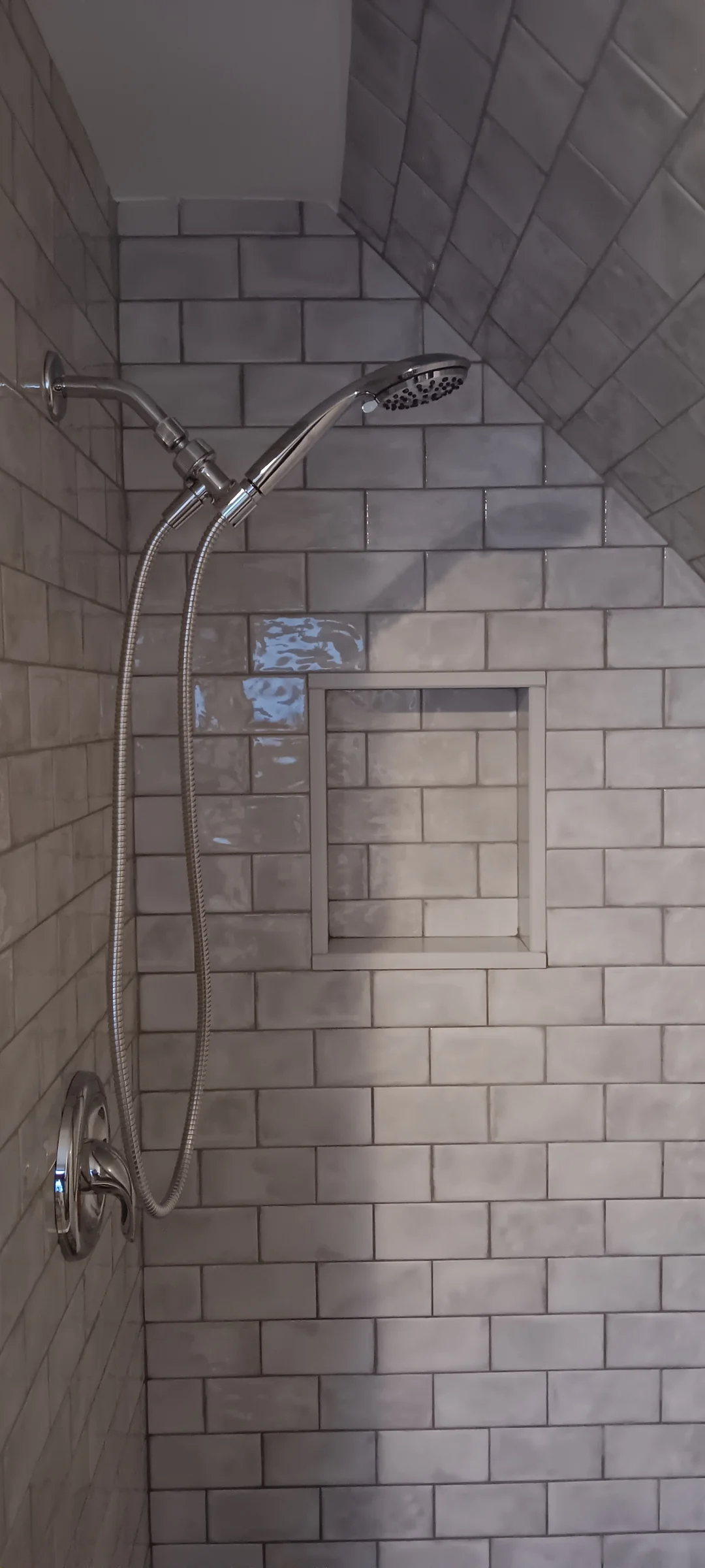 Glazed gray shower tiles around a recessed niche beneath a sloped ceiling.