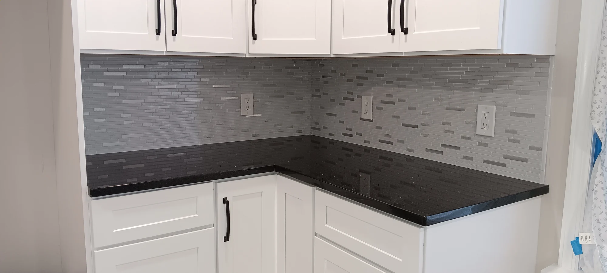 Gray mosaic kitchen backsplash above a dark countertop and white cabinets.