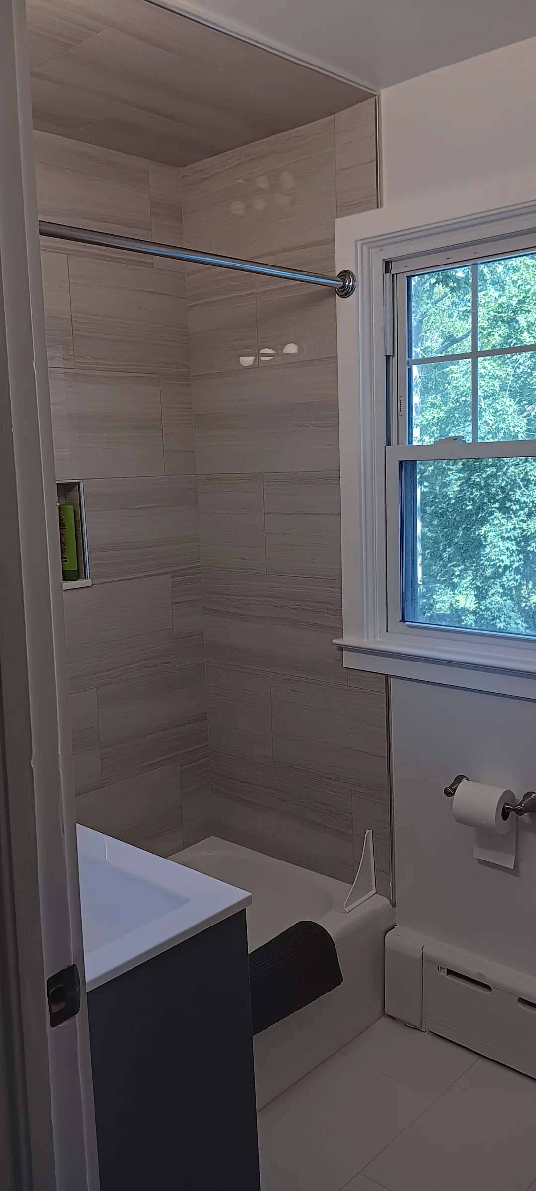 Neutral tile continuing across the bathtub walls and ceiling beside a window.
