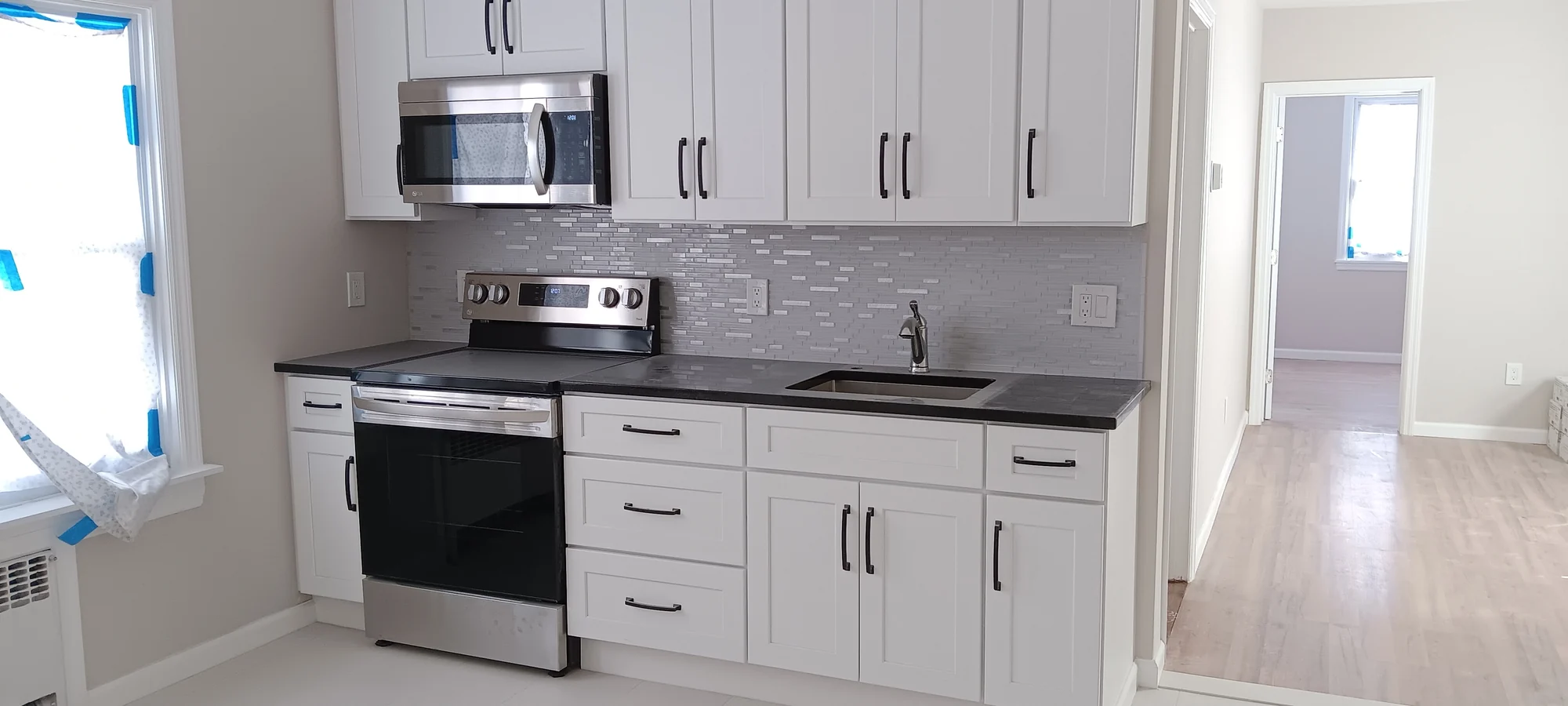 White kitchen cabinets, dark counters, and a gray mosaic backsplash during finishing work.