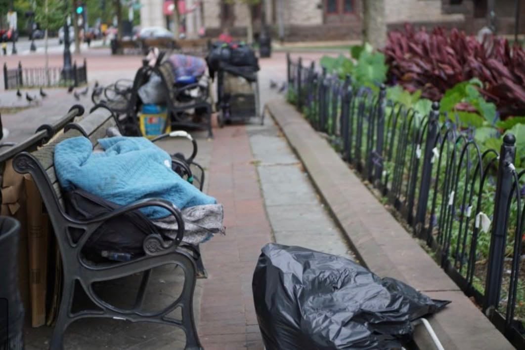 A person sleeping on a Copley Square bench with belongings