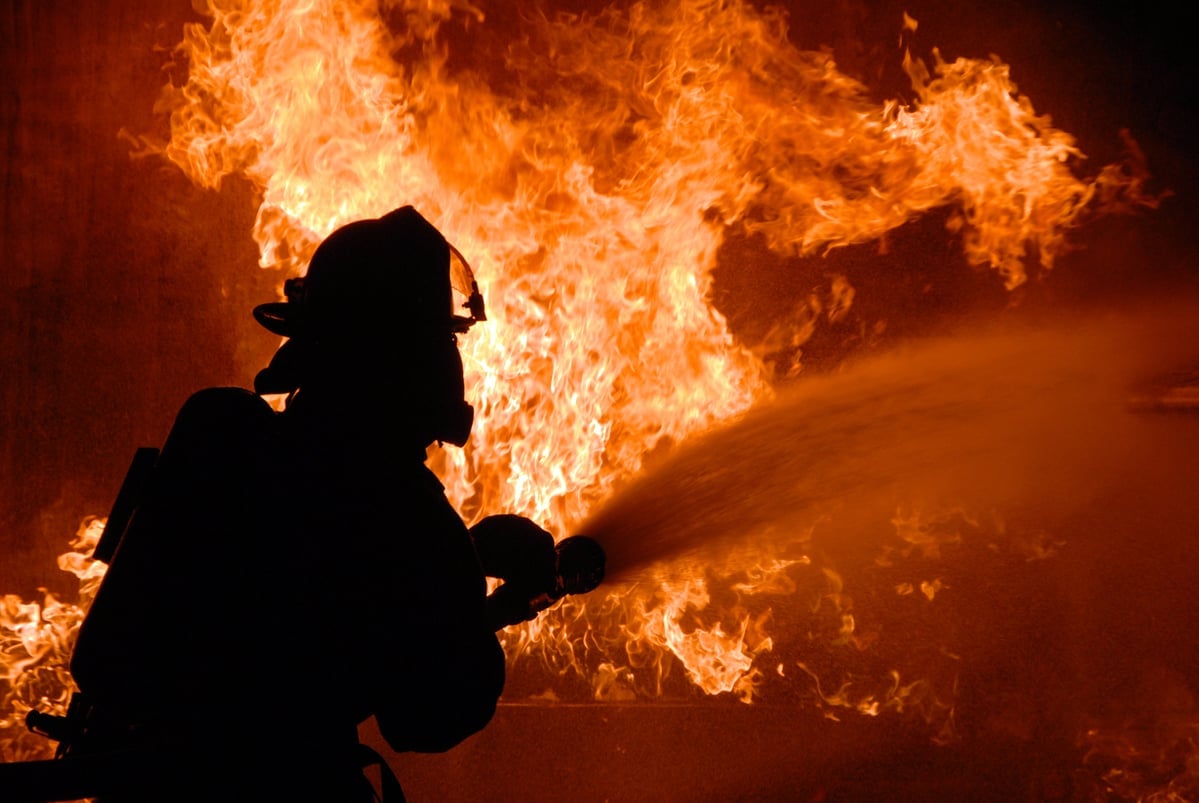 A firefighter spraying water on a wall of flames.