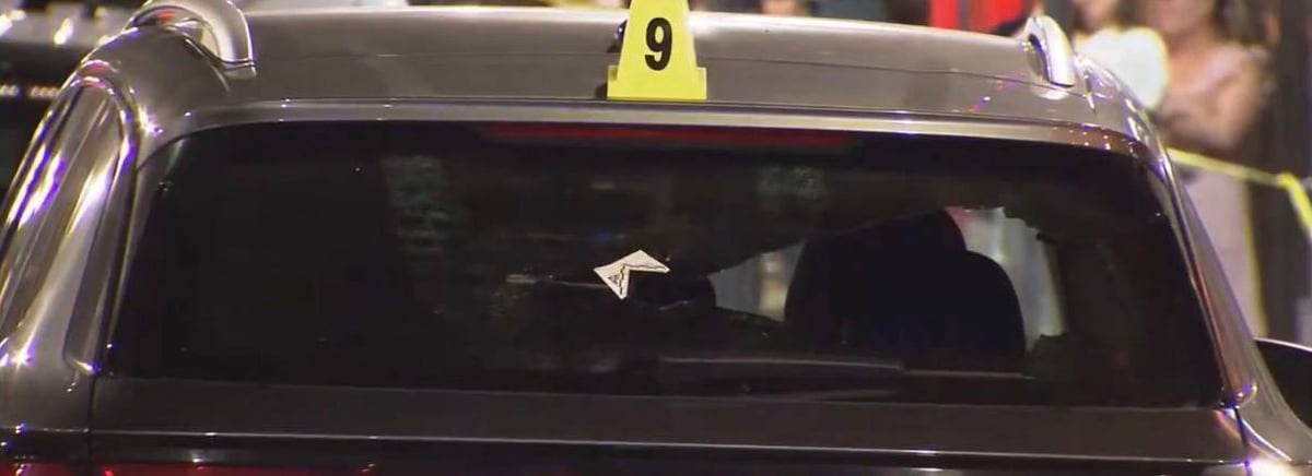 Black SUV with a bullet hole through the rear windshield and evidence marker on top.
