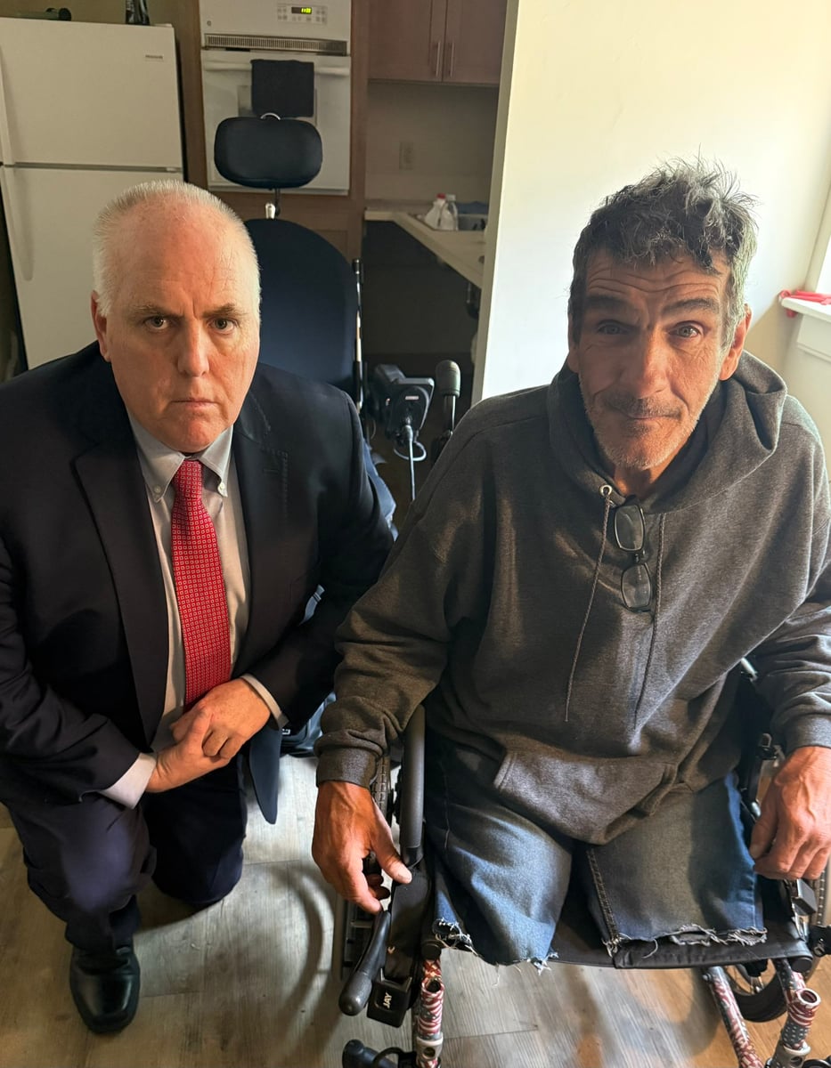 Boston City Councilor Ed Flynn kneeling next to Steve, a disabled veteran in a wheelchair, at his BHA Ruth Barkley apartment in the South End