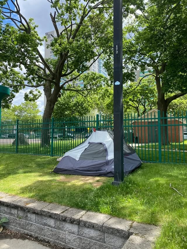 A gray dome tent pitched on the lawn of the Charles River Esplanade with a Back Bay high-rise behind it