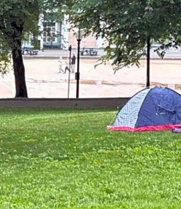 A blue and pink dome tent pitched on grass beside a paved sidewalk