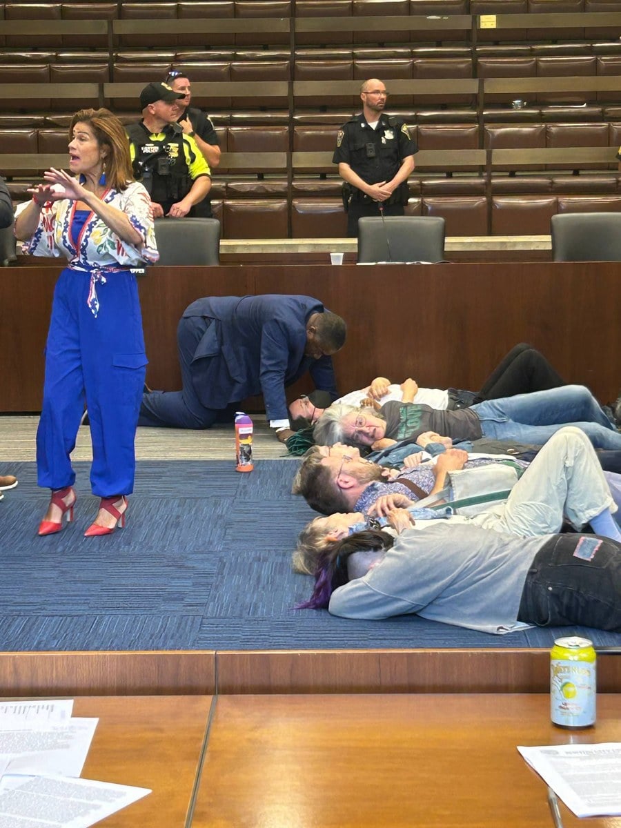 Boston Police officers stand on the dais as activists lay across the chamber floor in a die-in protest of Mayor Wu's youth-jobs cuts