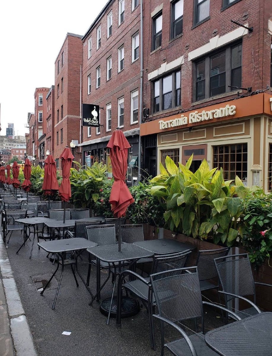 Terramia Ristorante's outdoor patio on a North End side street — closed red umbrellas, wrought-iron tables, planters of greenery in front of the restaurant.