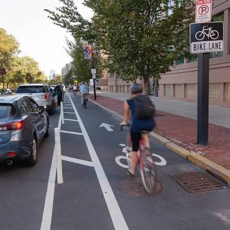 Cyclist riding in a protected bike lane in Boston, with a 'NO PARKING - BIKE LANE' sign prominently visible.