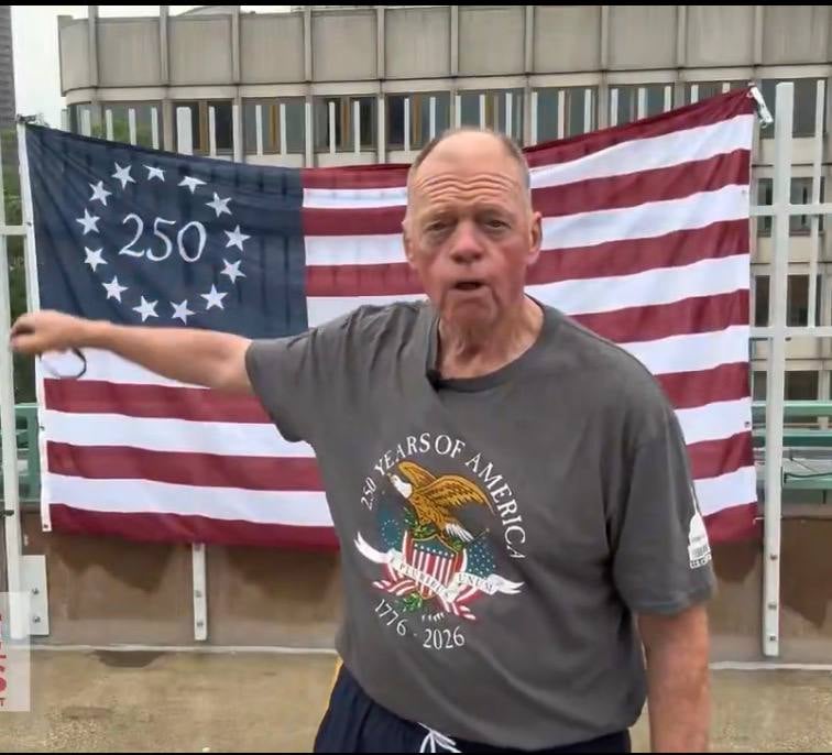 Congressional candidate Rob Burke at Boston City Hall Plaza on Friday, standing in front of his 13-star 250 commemorative American flag.