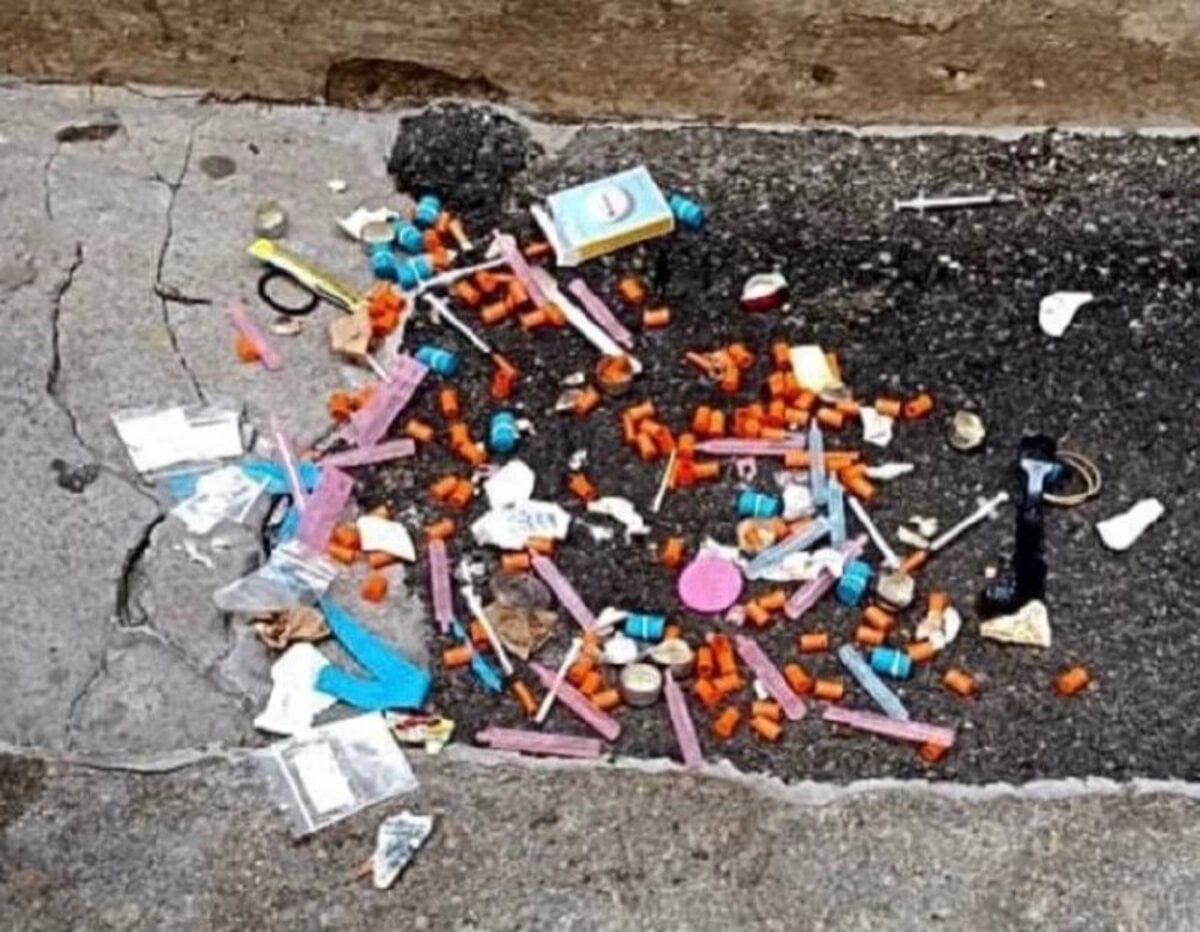 Dozens of brightly-colored syringe caps in orange, blue, and pink littering a Back Bay curb next to used needles and empty baggies.