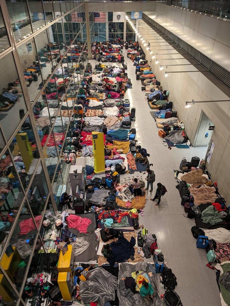 Migrant families sleeping on the floor at Boston Logan International Airport during Massachusetts's Emergency Assistance shelter overflow.