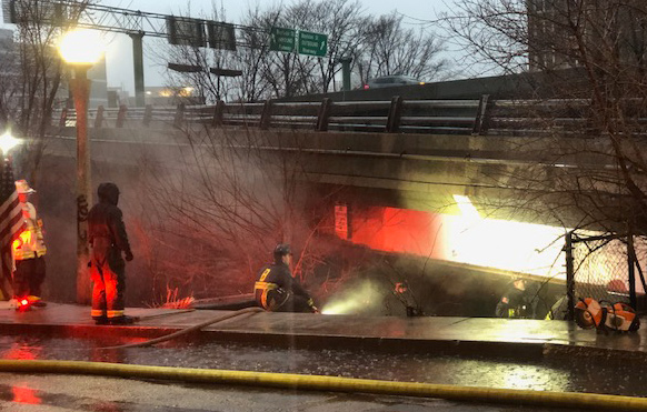 Firefighters battle flames under the Charlesgate East off-ramp in March 2024 after a blaze broke out beneath the bridge. Crews doused the fire and called in engineers to inspect for damage, highlighting the danger of encampments and stored fuel beneath one of Boston’s busiest bridges.