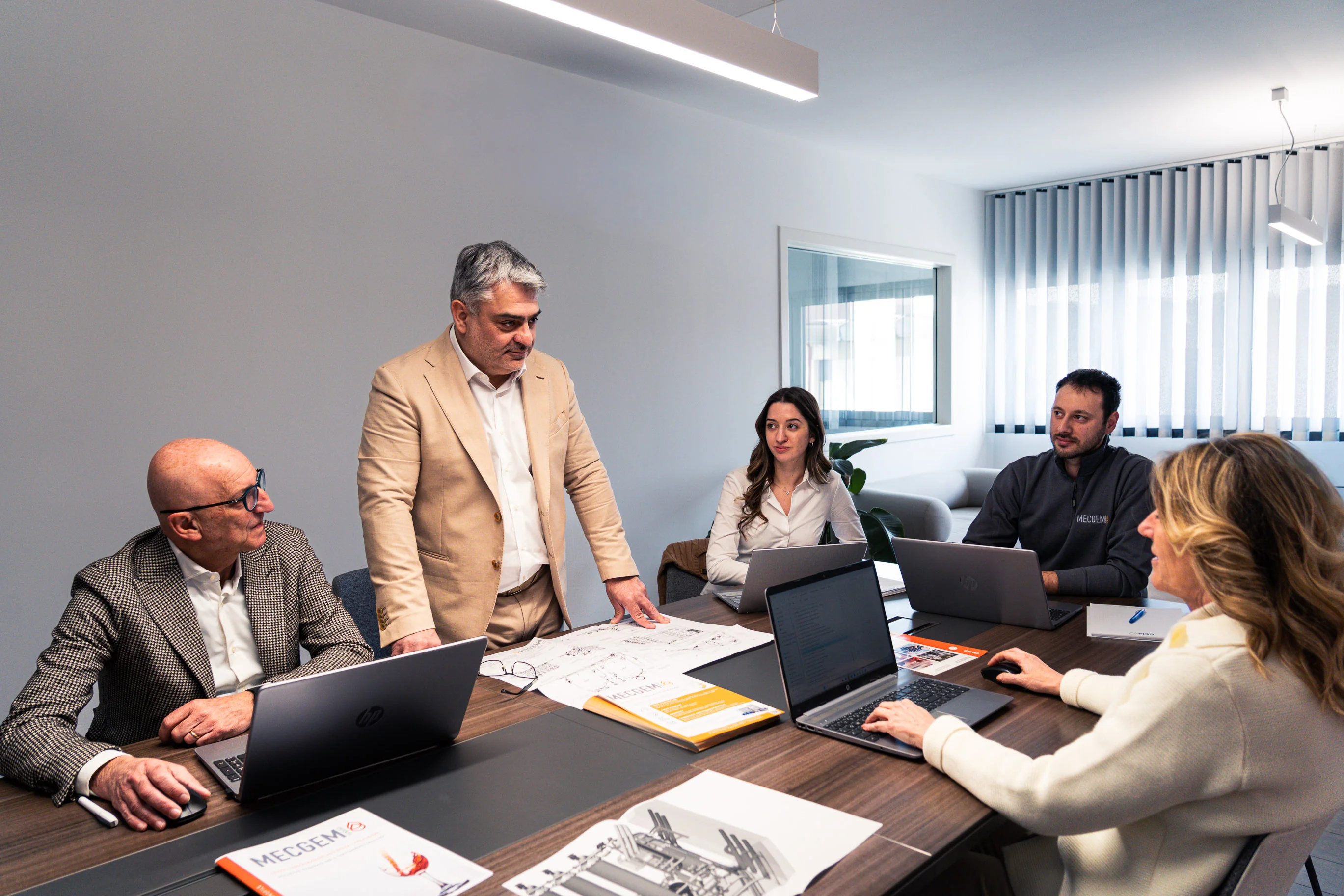 Direttore MecGem che spiega progetto tecnico al team nella sala riunioni