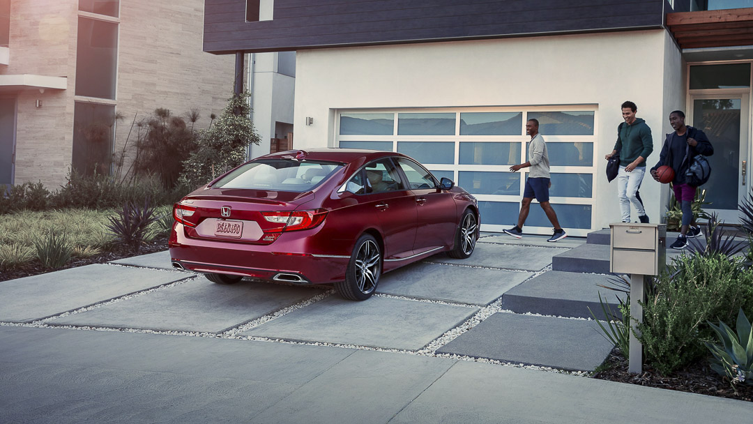 Honda Accord hybride usagée rouge devant une maison pour illustrer une berline hybride spacieuse et bien équipée.