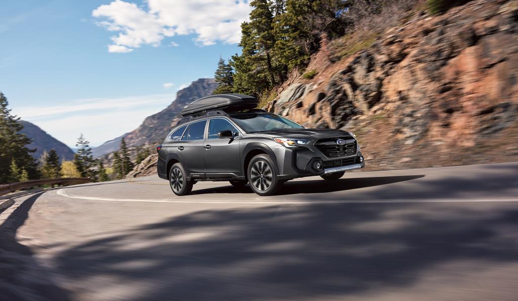 Subaru Outback AWD gris vu de trois quarts avant en conduite sur route de montagne, VUS intermédiaire à traction intégrale reconnu pour sa polyvalence et ses performances en toutes saisons.